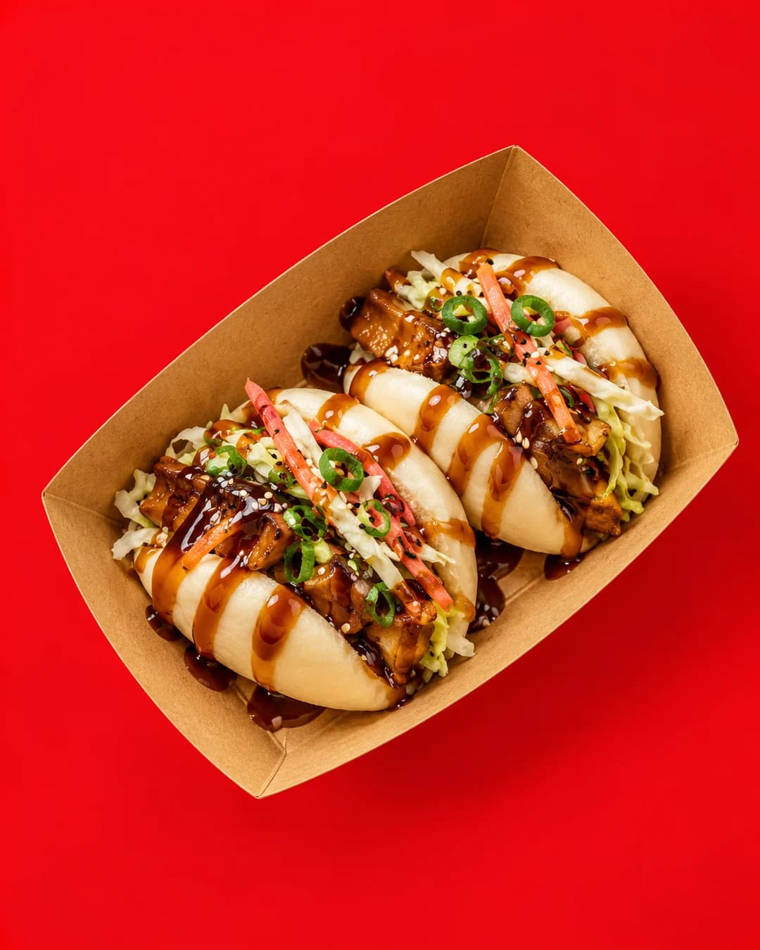 Two teriyaki veggie bao with slaw and chilli in a kraft tray