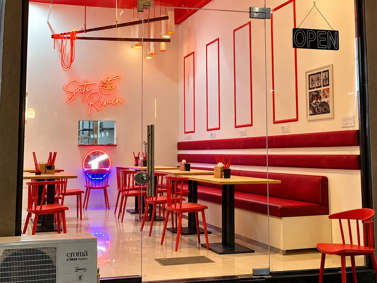 Glass-fronted SATO Gota with red booth seating, red chairs and a neon Sato Ramen sign