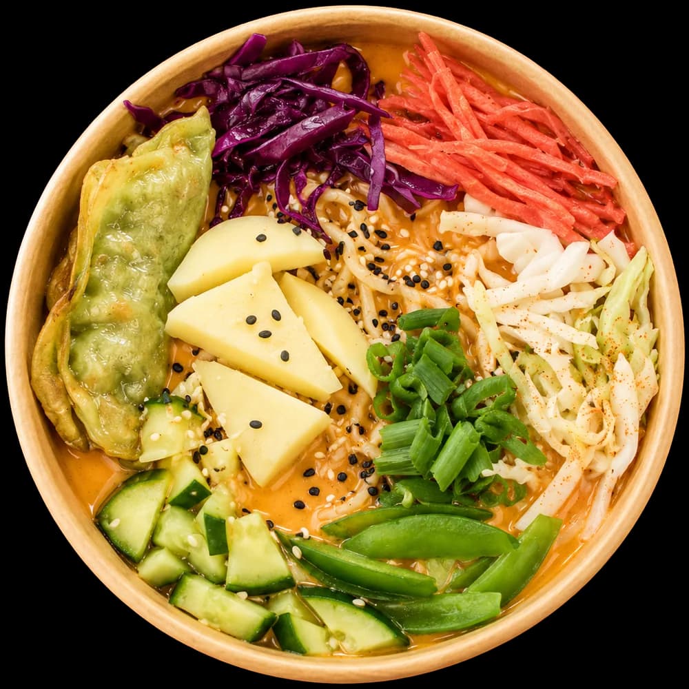 Top-down bowl of creamy ramen with cheese cubes, a dumpling, snap peas and spring onion