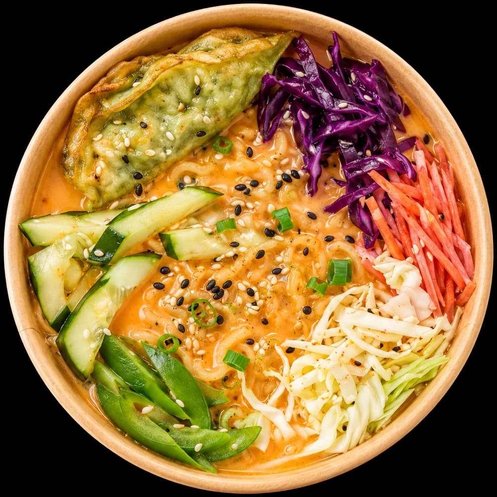 Top-down bowl of creamy veg ramen with a dumpling, cucumber, red cabbage and carrot