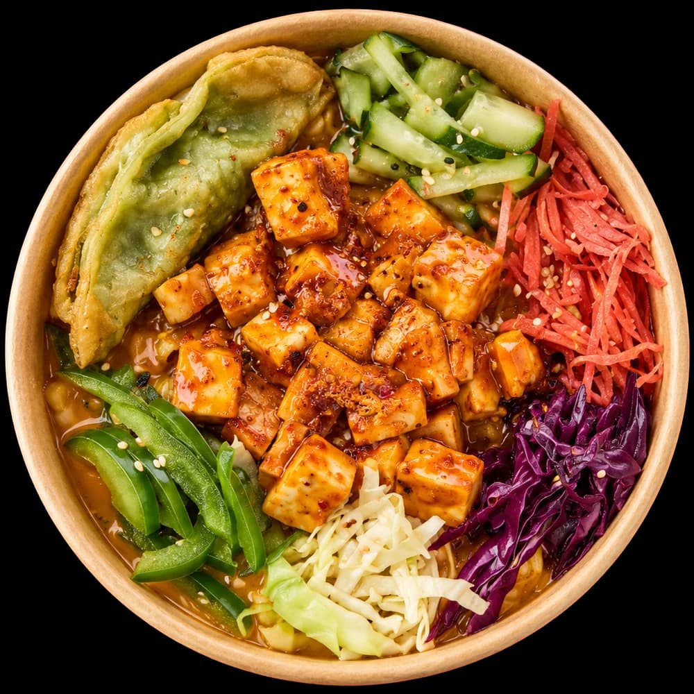 Top-down bowl of ramen with chilli-glazed tofu cubes, dumpling and pickled vegetables